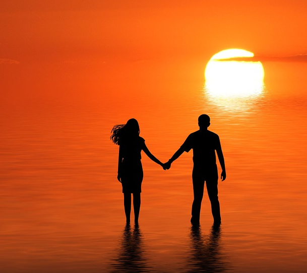 couple holding hands in the water at sunset